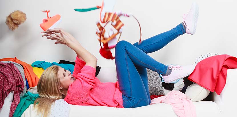 Junge blonde Frau beim Klamotten ausmisten auf einem weißen Sofa. Second Hand Wien.