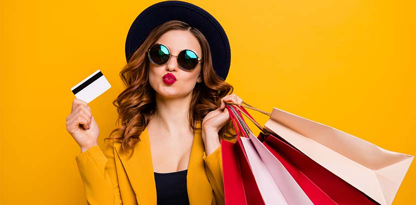 Hübsche brünette Shopaholic mit vielen bunten Einkaufstaschen und einer Kreditkarte.