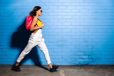 Junge Hipster-Frau mit pinkem Turnbeutel vor einer blauen Wand.