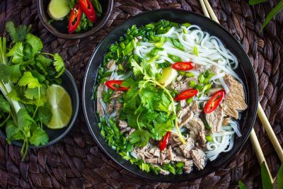 Eine Schüssel voller Pho mit Chili, frischem Koriander und Kräutern.