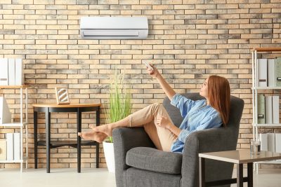 junge barfüßige Frau schaltet die Klimaanlage ein während sie zuhause auf ihrem Sofa sitzt