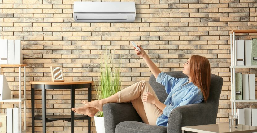 junge barfüßige Frau schaltet die Klimaanlage ein während sie zuhause auf ihrem Sofa sitzt