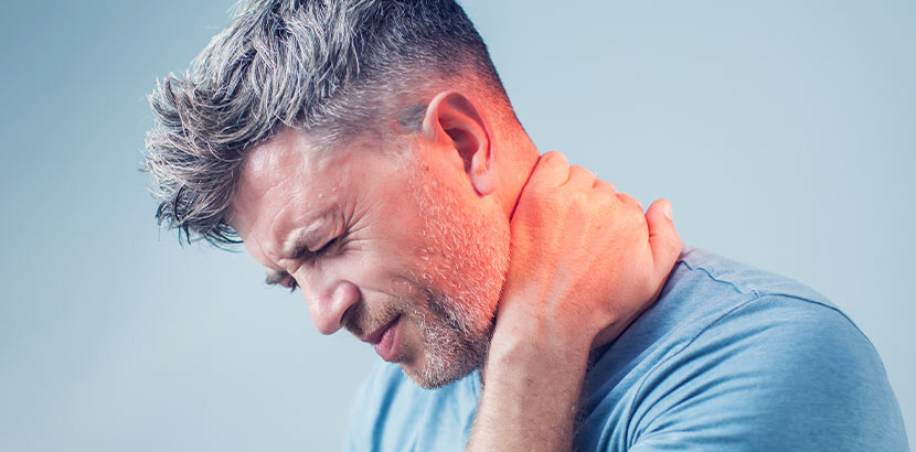 Mann mit grauen Schläfen und blauem Shirt, der sich den schmerzen Nacken hält. Kopfschmerzen und Migräne entwickeln sich häufig aus Verspannungen. Hier sind Hausmittel gegen Kopfschmerzen gefragt!