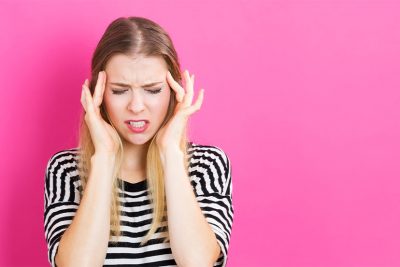 Junge Frau vor pinkem Hintergrund, die sich wegen Kopfschmerzen die Schläfen reibt. Hausmittel gegen Kopfschmerzen gefragt!