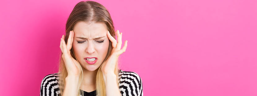 Junge Frau vor pinkem Hintergrund, die sich wegen Kopfschmerzen die Schläfen reibt.