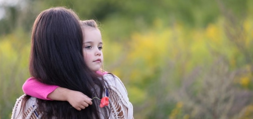 Kleines Mädchen im Arm seiner Mutter, das eine rote Mohnblume in der Hand hält und traurig schaut. Bestattungskosten Wien.