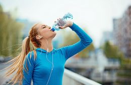 Eine schlanke Frau in Sport Kleidung trinkt viel wegen Hitze.