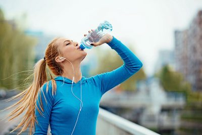 Eine schlanke Frau in Sport Kleidung trinkt viel wegen Hitze.