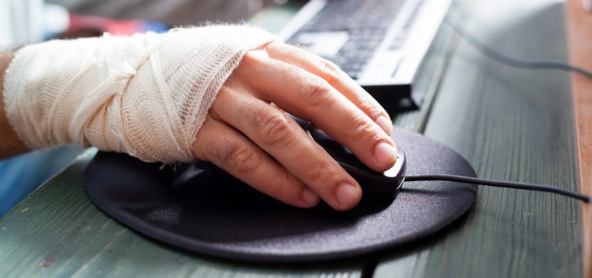Hand mit Verband, die eine Schreibtischmaus bedient. Ergonomie am Arbeitsplatz beugt solchen Verletzungen vor.
