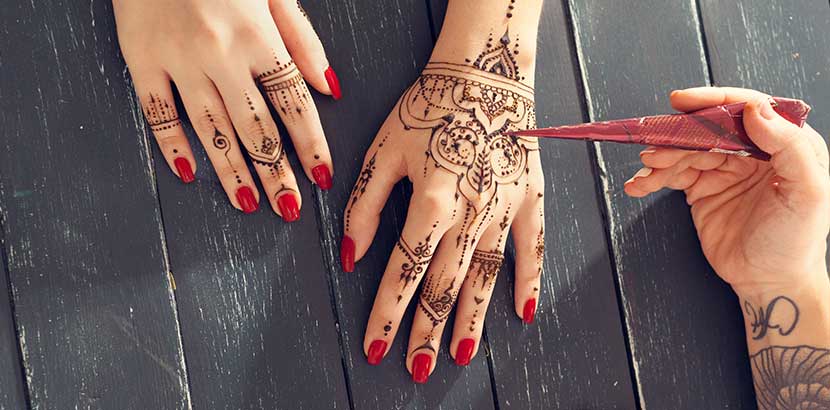 Hand einer Henna Künstlerin, die die Hände ihrer Kundin mit einem Henna Tattoo verziert.