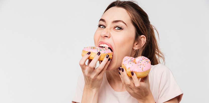 Junge hübsche Frau, die während ihrer Periode eine Fressattacke hat und zwei rosa Donuts verschlingt.