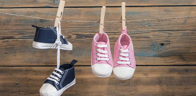 Zwei paar Baby Schuhe, ein blaues und ein rosanes, die an einer Wäscheleine hängen.