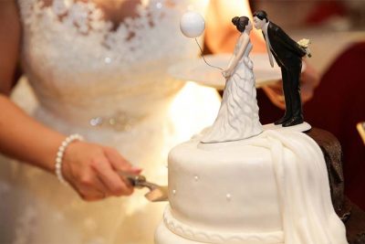 Braut, die gemäß der Hochzeitstradition die Hochzeitstorte anschneidet. Hochzeitsbräuche aus aller Welt.