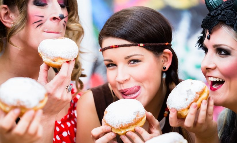 Gruppe junger hübscher Frauen, die zum Fasching Wiener Krapfen essen.