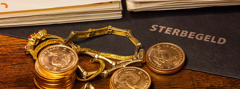 Goldschmuck, Münzen und große Geldscheine auf einer Mappe, in der die Sterbegeldversicherung aufbewahrt wird.