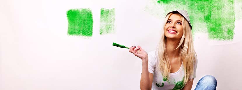 Junge blonde Frau, die eine Wand mit Wandlack in verschiedenen Farben gestrichen hat.