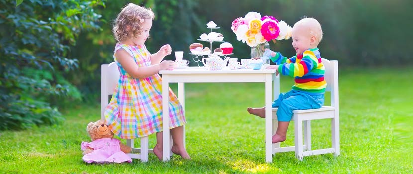 Gartenmöbel Kinder: Zwei Geschwister sitzen draußen auf Gartensesseln und spielen zusammen ein Garten Spiel.