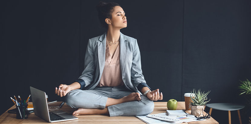 Geschäftsfrau, die im Büro auf dem Schreibtisch sitzt und meditiert. Meditation Wien.