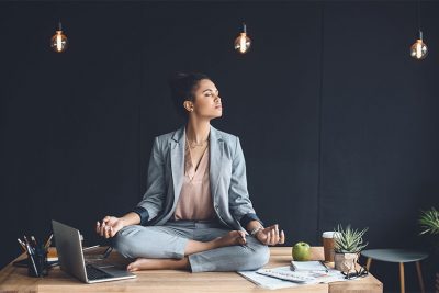 Geschäftsfrau, die im Büro auf dem Schreibtisch sitzt und meditiert. Meditation Wien.