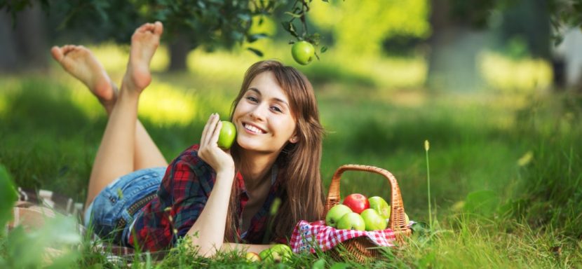 Junge Frau, die im Garten auf dem Rasen liegt und einen Apfel in der Hand hält. Worauf man beim Obstbäume schneiden achten muss.