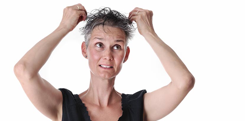 Frau im mittleren Alter, die ihr durch Haarausfall brüchig und dünn gewordenes Haar betastet.