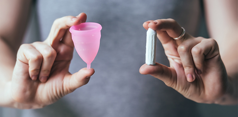 Eine Frau hält eine Menstruationstasse und einen Tampon.