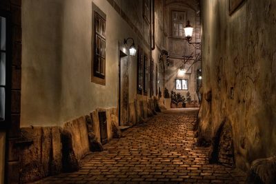 Dunkle Gasse im morbiden Wien, auf der schemenhafte Gestalten zu sehen sind.