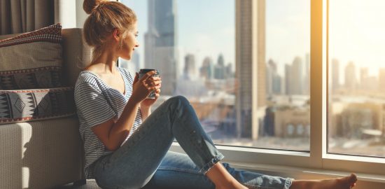 junge barfüßige Frau mit Dutt genießt Ausblick vor einem Schallschutzfenster