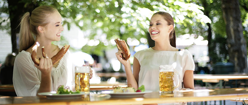Biergärten Wien: Zwei junge Frauen sitzen im Biergarten, trinken Bier und essen Brezln.