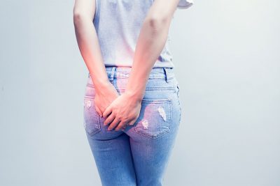 Rückenansicht einer jungen Frau, die sich den Po hält, weil sie Schmerzen hat. Hämorrhoiden Behandlung in Wien.