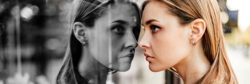 Junge Frau, die traurig ihr eigenes Spiegelbild im Schaufenster betrachtet. Sie leidet unter Depressionen.