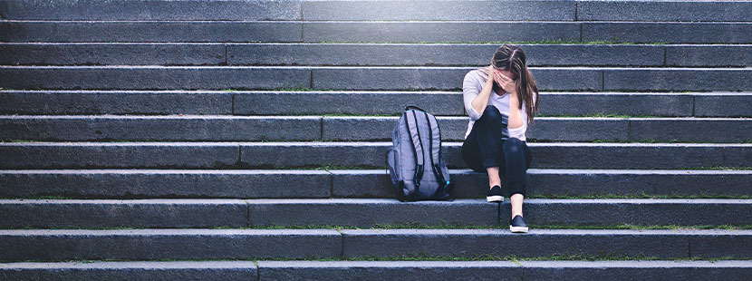 Mädchen weint in der Schule alleine auf einer Treppe. Mobbing in der Schule.