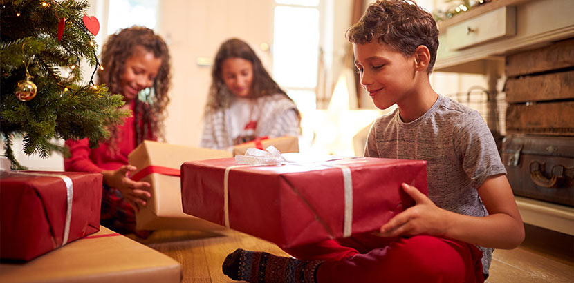 9-jähriger Junge unterm Weihnachtsbaum mit einem großen Geschenkpaket.