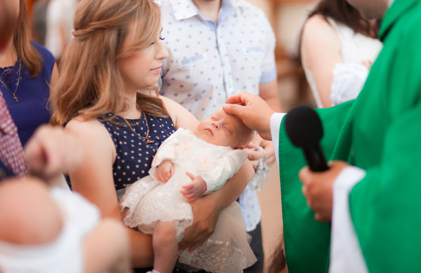Der Pfarrer segnet das Baby bei einer Taufe. Dabei wird es von der Taufpatin gehalten.