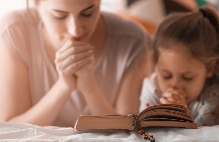 Eine Taufpatin und ihr Patenkind lesen die Bibel und beten zusammen.