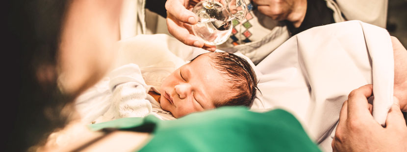Ein Baby wird von einem Pfarrer mit Taufwasser getauft.