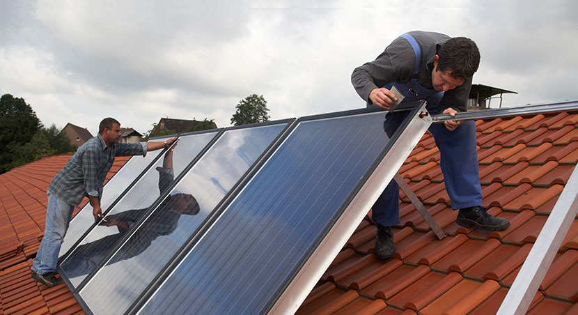 Zwei Installateure montieren Sonnenkollektoren für eine Solarthermieanlage auf einem Dach.