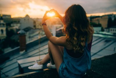 Eine Frau sitzt auf dem Dach, während die Sonne untergeht.