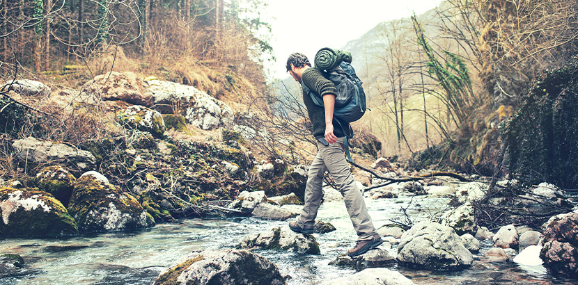 Junger Mann mit Wanderrucksack, der einen Fluss überquert. Außergewöhnliche Geschenke.