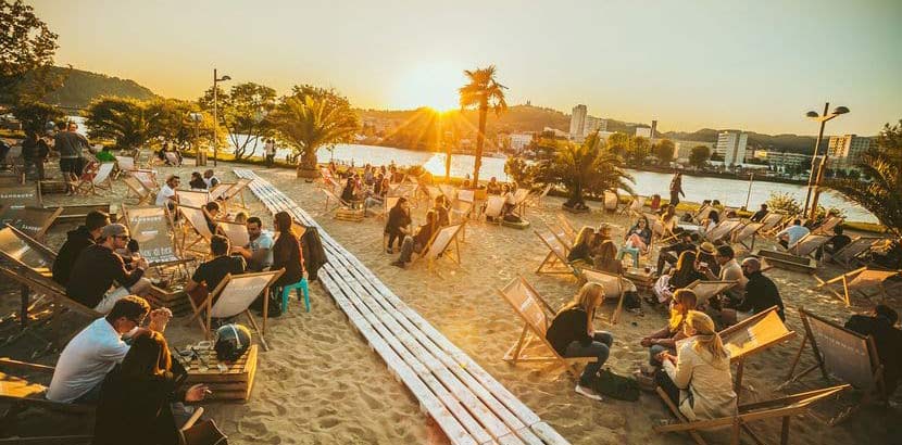 Menschen in Strandliegen bei Sonnenuntergang in der Strandbar Sandburg. Cocktailbar Linz