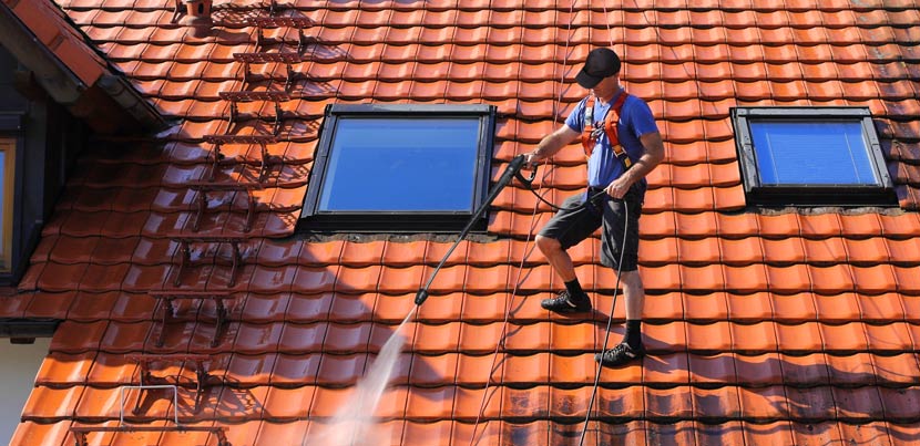 Ein Mann, der bei einer professionellen Dachreinigung mit dem Hochdruckreiniger auf dem Dach steht