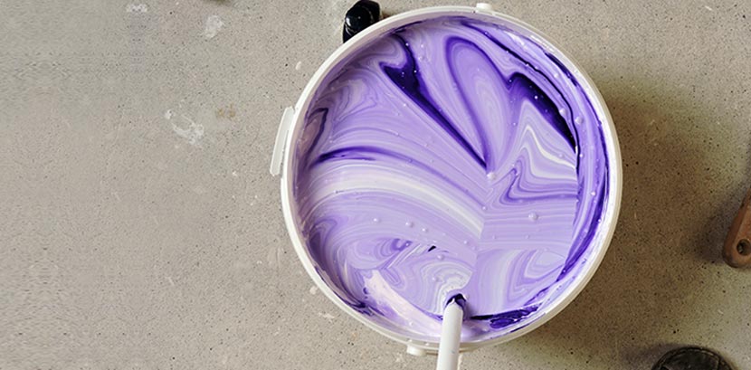 Ein Farbeimer in dem weiße und lila Farbe vermischt werden.