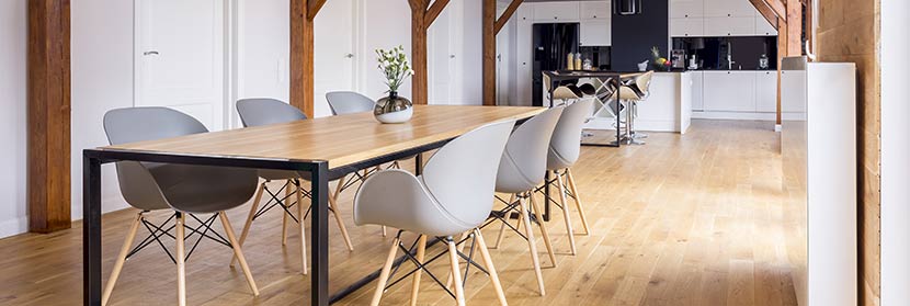 Ein Raum mit einem großen Holztisch, modernen, hellgrauen Stühlen und einem hellen Dielenböden.