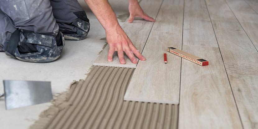 Ein Fliesenleger verlegt helle Fliesen in Holzoptik.