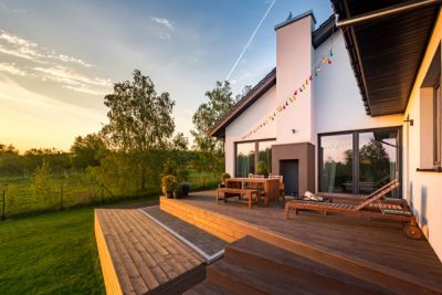 Wunderschöne Holzdielen Terrasse mit zwei Ebenen in grüner Landschaft vor einem malerischen Himmel bei Sonnenuntergang.