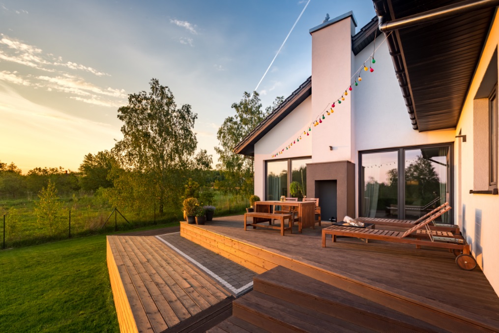 Wunderschöne Holzdielen Terrasse mit zwei Ebenen in grüner Landschaft vor einem malerischen Himmel bei Sonnenuntergang.