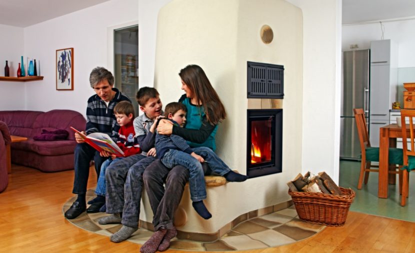 Glückliche Familie mit drei Kindern, die es sich auf der Sitzbank ihres Kachelofens gemütlich gemacht haben.