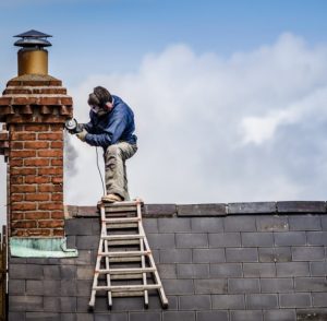 Ein Rauchfangsanierer, der am Dach steht und prüft, ob man an dem Rauchfang eines alten Hauses einen Kachelofen anschließen kann.