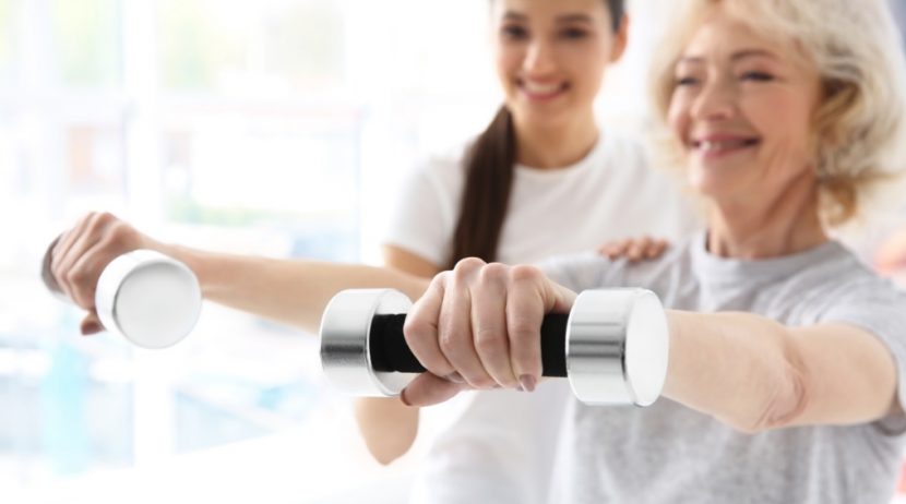 Junge dunkelhaarige Physiotherapeutin, die Hanteltraining mit einer älteren Patientin macht.