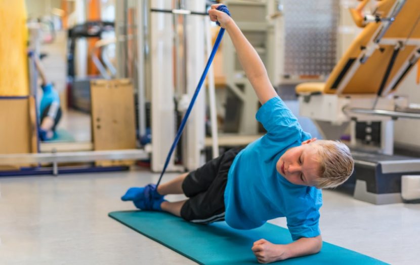 Blonder Junge, der mit Physiotape auf einer Gymnastikmatte trainiert. Physiotherapie Linz.